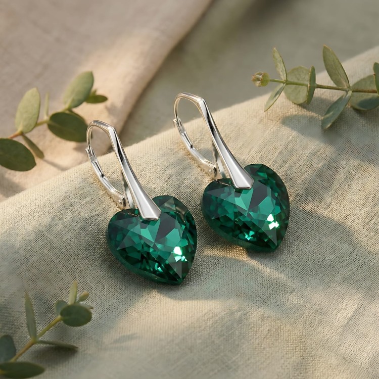 Srebrne kolczyki z kryształami serca Emerald w zbliżeniu. Zdjęcie eksponuje szlif i kontrast koloru z jasną oprawą.