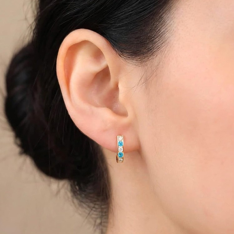Zbliżenie niebieskich i jasnych cyrkonii w złotych kolczykach 585